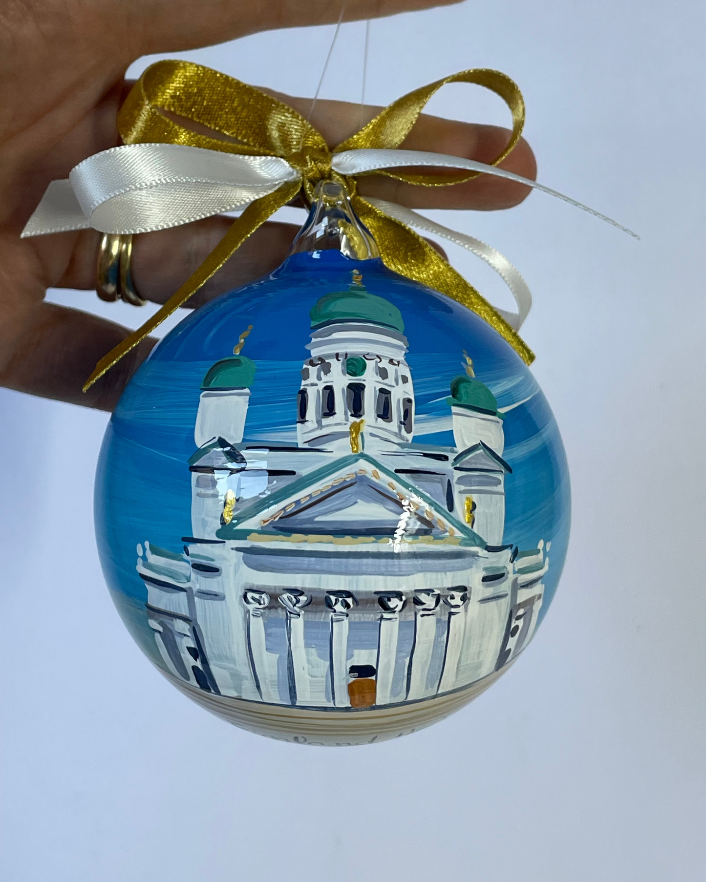 Hand holding hand-painted glass ornament – Helsinki Cathedral with green domes, Finland travel souvenir