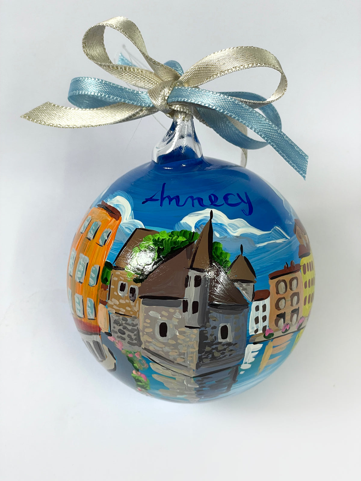 Hand-painted glass ornament – Annecy inscription with Palais de l'Isle stone tower, colourful buildings, snow-capped mountains and turquoise canal reflections, blue and gold ribbon, France souvenir