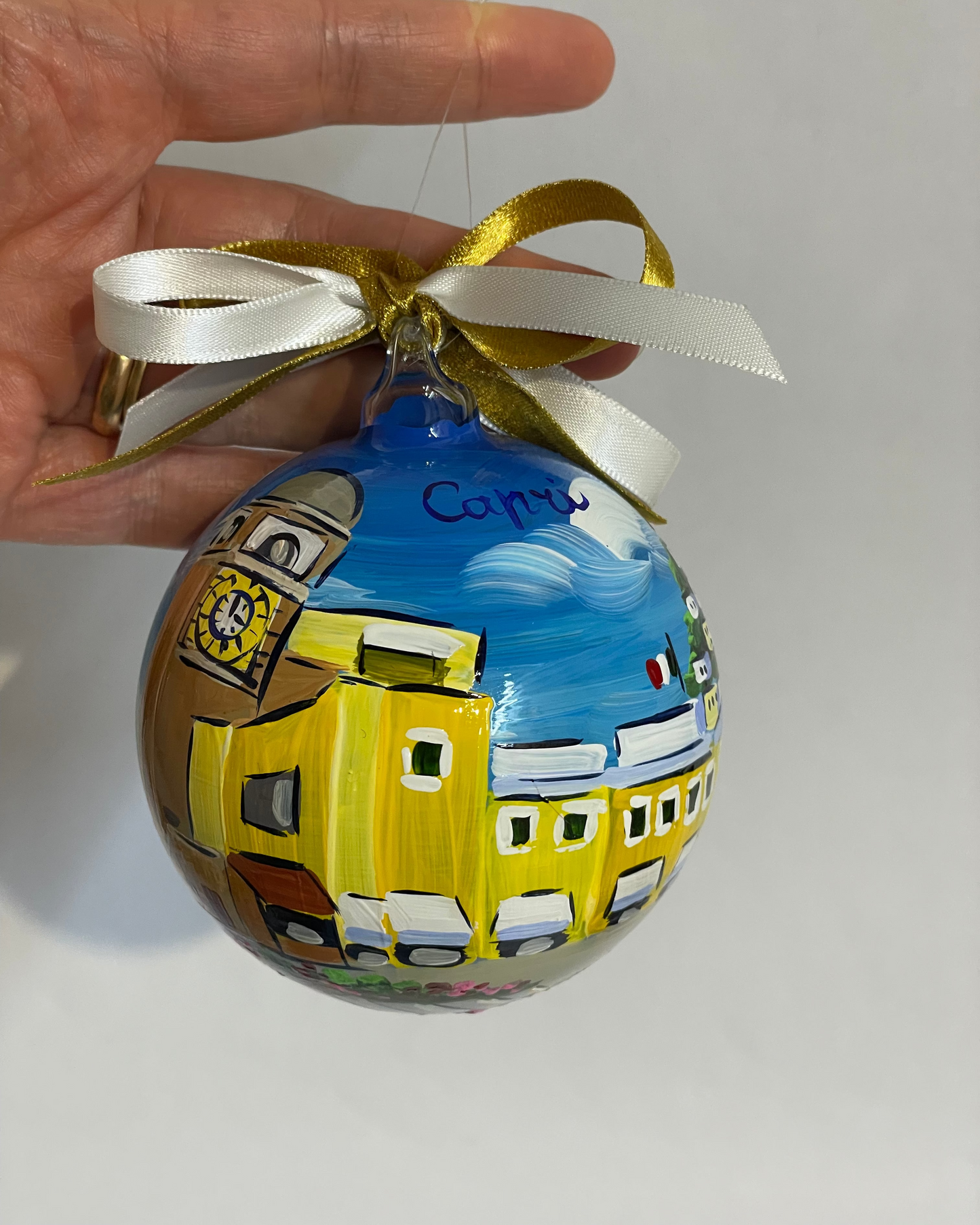 Hand holding hand-painted glass ornament – Capri Piazzetta clock tower and yellow buildings, Italy travel gift