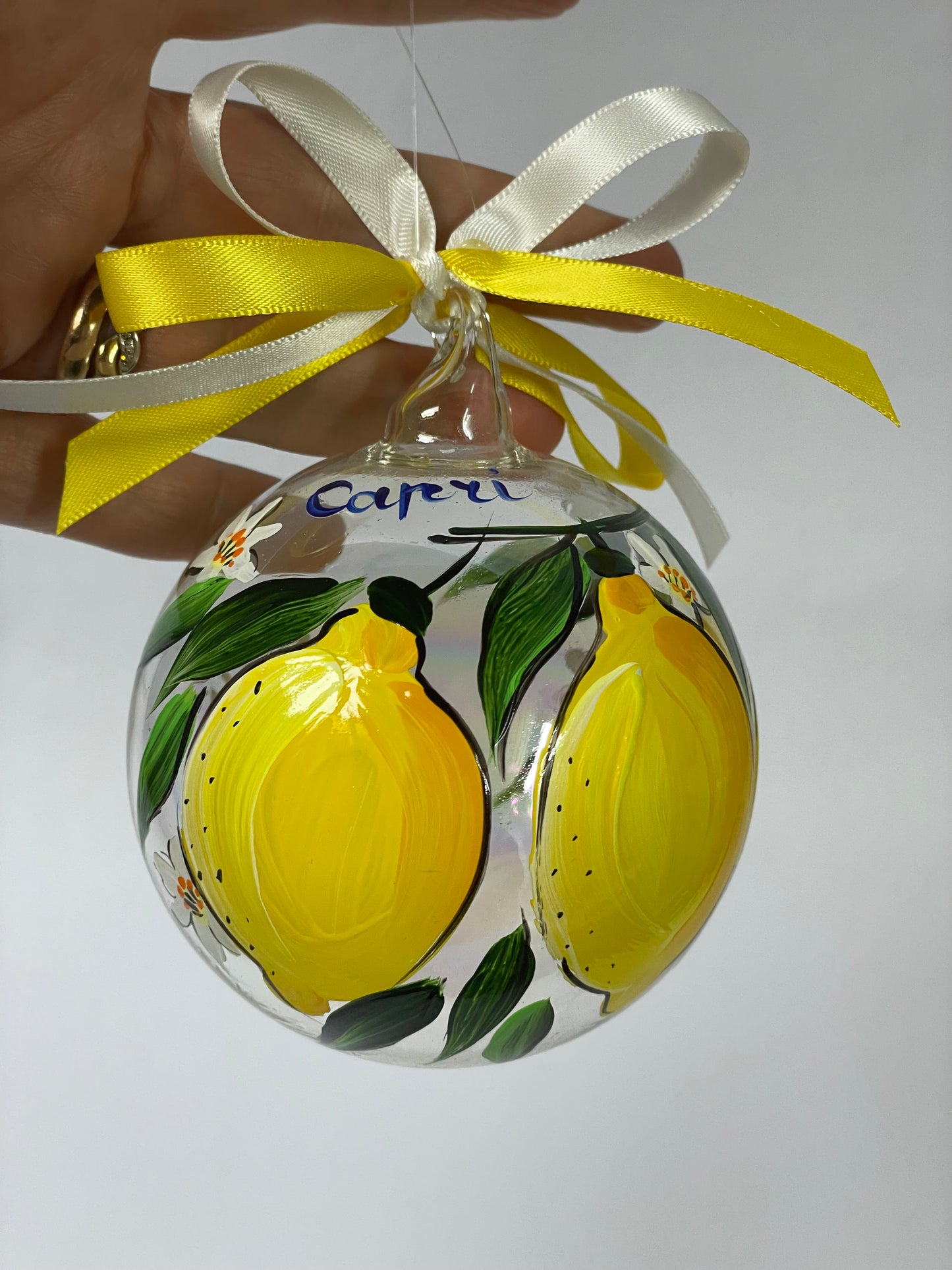 Hand holding hand-painted glass ornament – Capri lemon tree with yellow lemons and white flowers, white ribbon