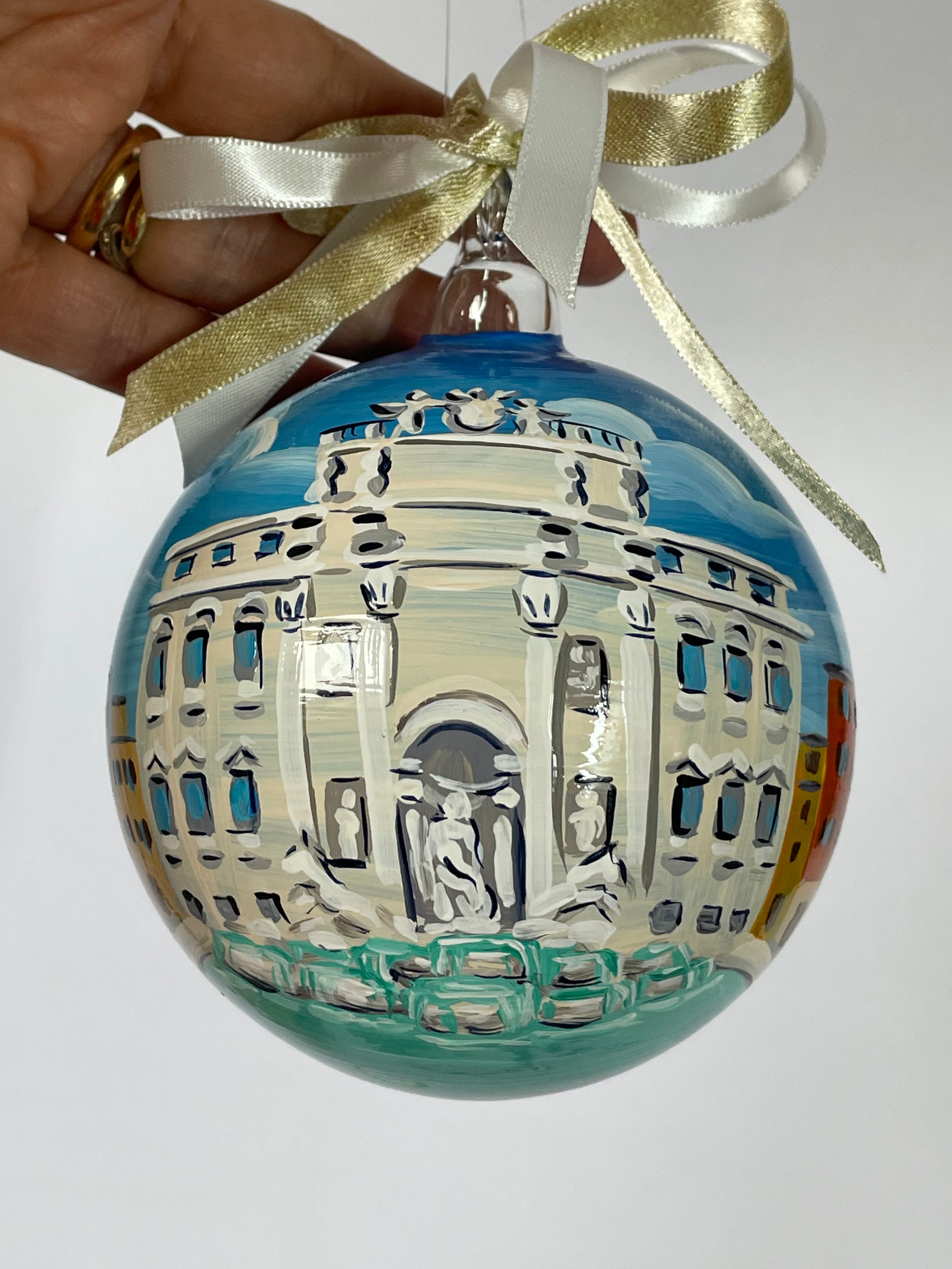 Hand holding hand-painted glass ornament – Trevi Fountain front view with Neptune statue, baroque palace and turquoise basin