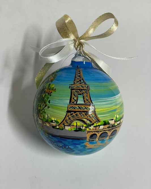 ornamento in vetro dipinto a mano che raffigura Parigi, la torre Eiffel, un ponte sula Senna. Il cielo sullo sfondo è sfumato dal blu al giallo.